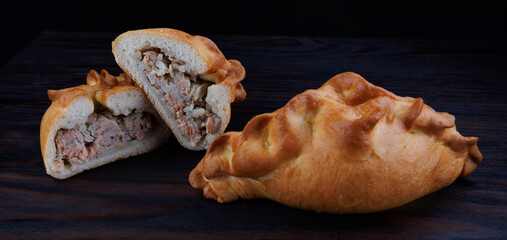 Rastegai, Russian fish pie. Pie with red fish and rice on a dark background. Whole and cut fish pie.