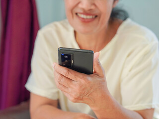 Lifestyle Health Care Concept. Asian senior woman sitting playing her mobile phone with a fun and happy expression. Elderly person using technology to relax on a day off. Good mental health in old age