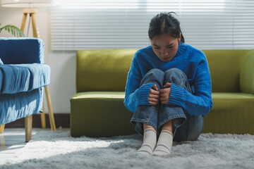 Young woman sitting on a soft carpet in a living room, appearing deep in thought. Natural light...