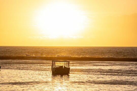Serene sunset with silhouetted boat on ocean. - Powered by Adobe