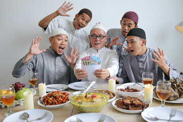 Senior Muslim Man Showing Money On Envelope or THR And His Family Surprised on Celebrating Eid Al Fitr