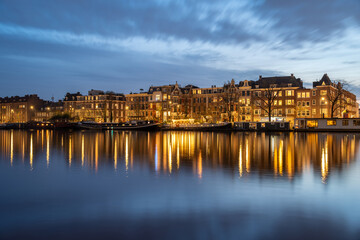 Naklejka premium Amsterdam Diamantbuurt and Amstel river at sunset, waterfront with houseboats and typical dutch houses reflected in the water surface