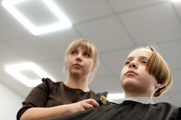 Fototapeta premium Child receiving haircut from stylist in modern barber shop during daytime