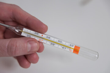 Mercury thermometer in hand shows temperature 37.3 on a white background close-up 