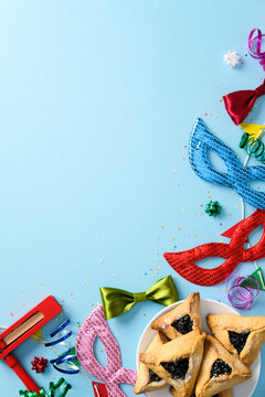 Jewish Carnival holiday Purim celebration concept. Flat lay hamantaschen cookies, masquerade masks, and colorful party decorations on a blue background