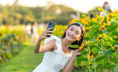Asian woman in white dress using smartphone at sunflower garden. Young woman enjoying peaceful...