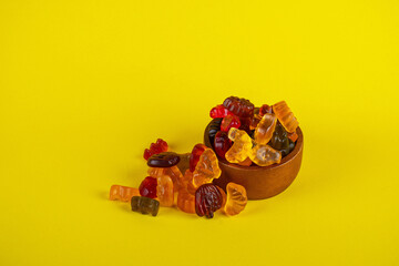 Fruit flavored worm shape, jelly candies in wood cup. Isolated on yellow background.