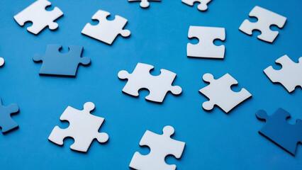 Naklejka premium Scattered puzzle pieces against a blue background. The pieces are a mix of white and blue.