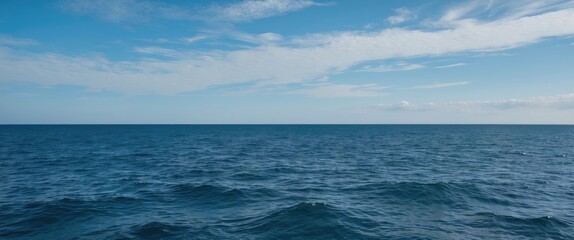 Fototapeta premium Calm ocean waters under a clear blue sky with scattered clouds and gentle waves copy space