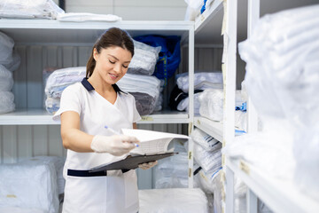 Female laundry worker checking inventory of clean clothing in dry cleaner storage room.
