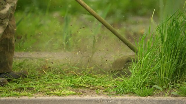 gardener with grass trimmer mows lawn in slow motion