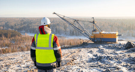 Industry coal mining, worker observes machinery in snowy open pit mine