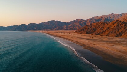 Fototapeta premium Ocean waves reaching sandy shore against mountains at sunrise, for vacation ads
