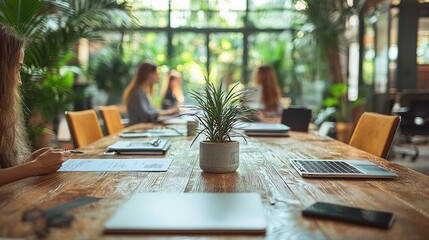 A collaborative workspace with plants, laptops, and people engaged in discussion.