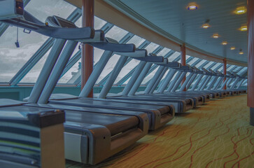 Fototapeta premium Moderne Fitnessgeräte und Kraftmaschinen in Sportstudio auf Kreuzfahrtschiff - Modern cardio and weight equipment in fitness center gym onboard cruiseship cruise ship liner