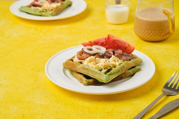 Breakfast, spinach waffles with egg salad, pickled herring and fresh tomato on a white plate on a yellow concrete background. Waffle recipes.