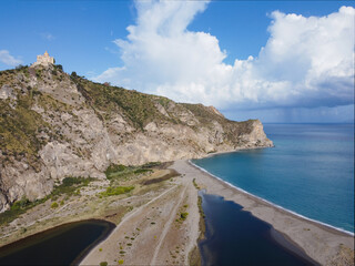 Aerial drone view of Laghetti di Marinello, natural reserve in Sicily, Italy. Sand strip with crystal clear turquoise lagoons, lush Mediterranean vegetation, below a cliff and Tindari Sanctuary.