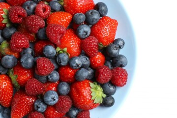 Different fresh ripe berries in bowl on light table, top view