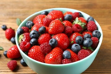 Different fresh ripe berries in bowl on wooden table