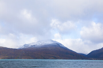 Autumn landscape of the Lyngen Alps in Northern Norway with snowy peaks, dramatic clouds, and a tranquil fjord.