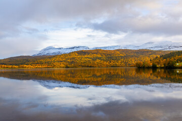 Fototapeta premium Autumn landscape of Northern Norway, with colorful trees, serene water reflections, and dramatic mountains.
