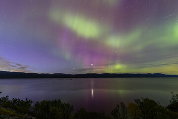 Northern lights in Kiruna, Sweden, reflecting on calm water in September with stars and forest in the background.