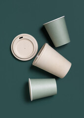 New light green paper cups and reusable bamboo coffee cup on a dark green top view, mockup
