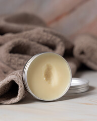 Opened body butter jar near light brown bath towel close up, herbal cosmetics for bodycare