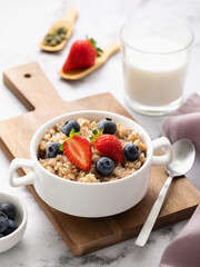 Buckwheat flakes with strawberries and blueberries in a ceramic white plate on a wooden tray, healthy breakfast