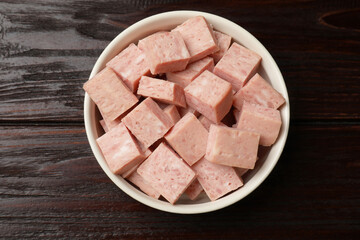 Pieces of canned meat in bowl on wooden table, top view