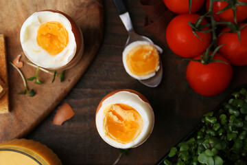 Soft boiled eggs, microgreens and tomatoes on wooden table, flat lay