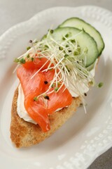 Delicious bruschetta with salmon, cream cheese and cucumber on light table, closeup