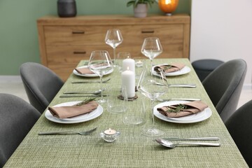 Stylish table setting with olive tablecloth, glasses and candles indoors