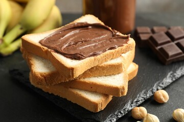 Sandwich with chocolate butter, hazelnuts and bananas on black table, closeup