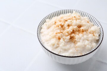 Tasty rice pudding with cinnamon on white tiled table, closeup