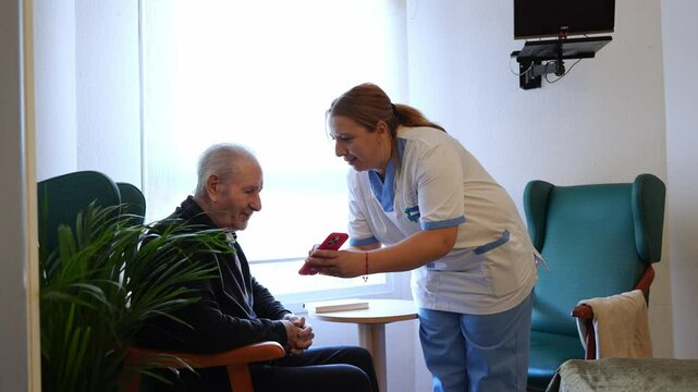 Nurse attentively helps elderly man with a smartphone, showcasing compassionate care in a nursing home environment