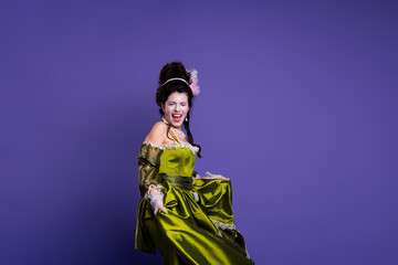 Obraz premium Young woman in an elegant green dress with a historical aristocratic theme posing against a purple background
