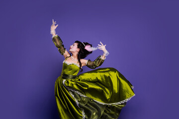 Elegantly styled woman in green baroque dress posing against purple background showcasing a historical and regal theme