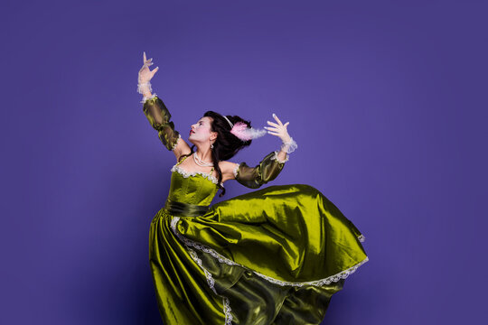 Elegantly styled woman in green baroque dress posing against purple background showcasing a historical and regal theme