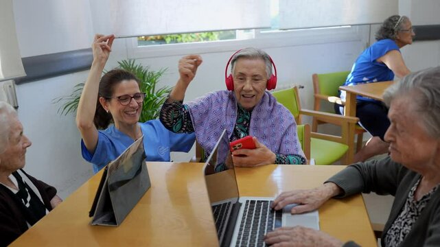 Elderly residents and a caregiver share a joyful moment, listening and dancing to music in a nursing home setting, using modern technology to connect