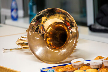 French horn with reflections on its bell, placed on a table with muffins in the foreground