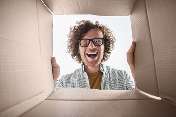 A happy man enthusiastically opens a cardboard box, expressing joy and excitement. The image...