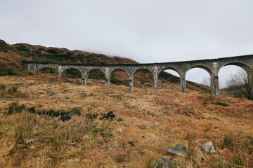 Fototapeta premium Glenfinnan Viaduct arches gracefully over rugged Scottish landscape in misty weather