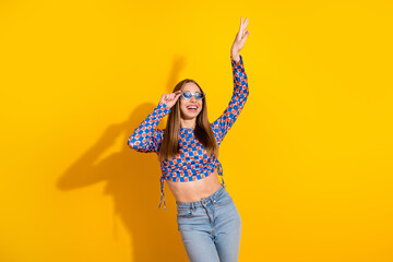Cheerful young woman posing stylishly with sunglasses against bright yellow background in casual fashion attire