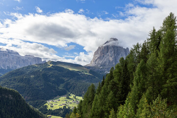 Sassopiato mountain towers above green valleys and forests under a bright sky, creating a peaceful alpine landscape in the Dolomites