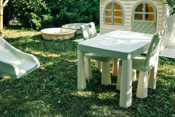 Children's backyard play area with a plastic slide, sandbox, table, chairs, and a small playhouse on the lawn. Perfect for outdoor fun, summer activities, and family entertainment