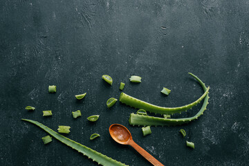 Fresh aloe vera gel in a wooden spoon with cut aloe leaves on a dark textured surface. Natural...