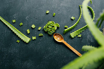Fresh aloe vera gel in a wooden spoon with cut aloe leaves on a dark textured surface. Natural...
