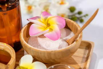 Close up of spa salt scrub in wooden bowl with frangipani flower for skincare and relaxation