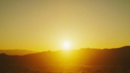 Fototapeta premium A glowing horizon at sunset casts a warm golden light over blurred mountains, evoking a sense of peace and tranquility.